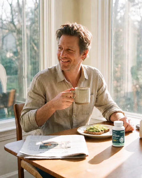 A man smiles over coffee and toast at a sunny breakfast table, a bottle of Daily Probiotic 20B beside his plate.
