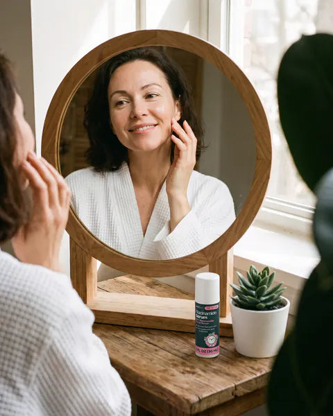 A woman in a robe dabs serum onto her cheek at a vanity table, a bottle of Niacinamide Serum beside her.